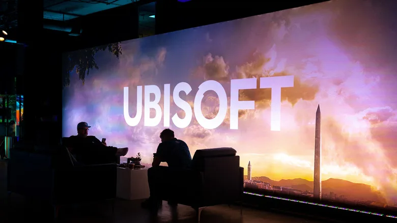 Two people sitting in shadow in front of a large Ubisoft logo.