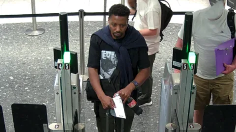 A CCTV image shows a man walking through a passport gate