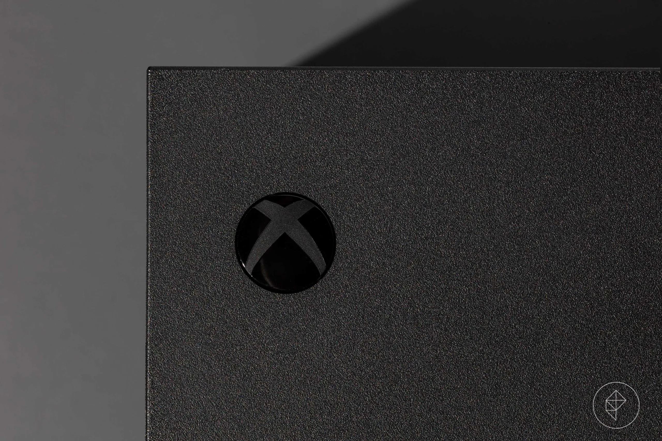 close-up of the Xbox power button on an Xbox Series X video game console photographed on a dark gray background