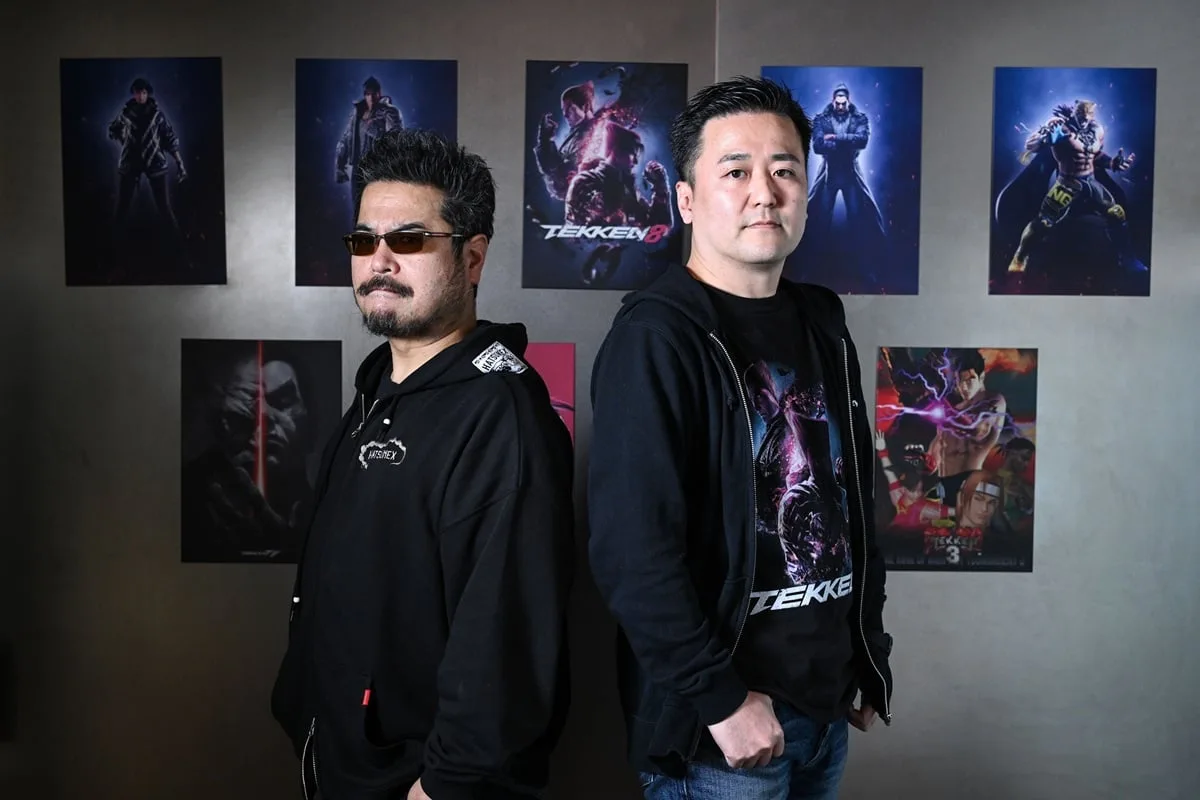 Kohei Ikeda and Katsuhiro Harada stand in front of Tekken posters.
